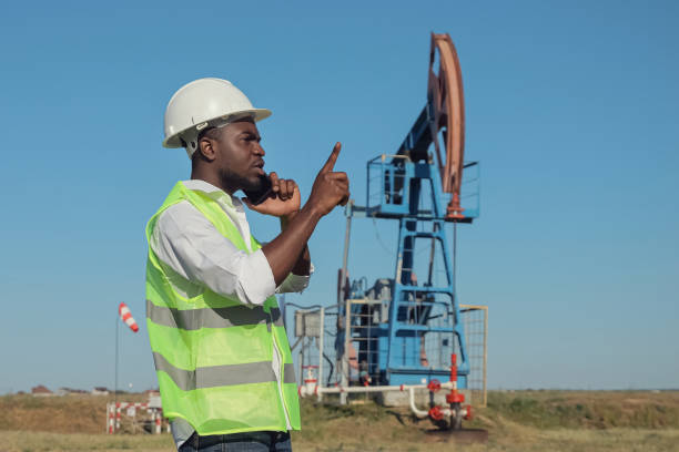 African American engineer talks on phone with colleague about balanced pumping unit producing crude oil. Black ceo controls jack-pumps operation