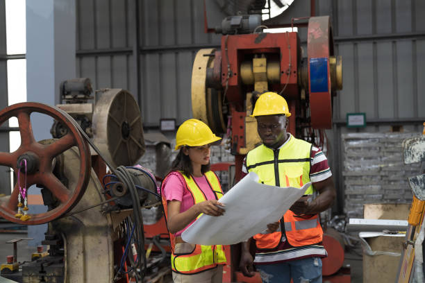 Manufacturing industrial concept. Male and female engineer workers working at manufacturing production lines in factory during manufacturing process, wearing safety uniform and use digital tablet