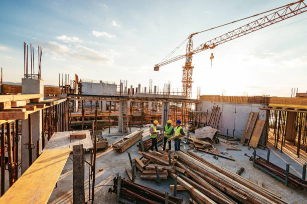 Construction industry concept - architects and engineers discussing work progress between concrete walls, scaffolds and cranes.